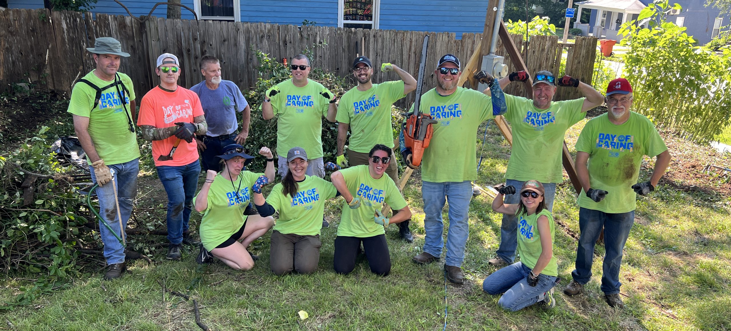 A group of O'Reilly team members, dressed in volunteer tshirts flex their muscles after clearing a backyard during the United Way's Day of Caring in 2024.