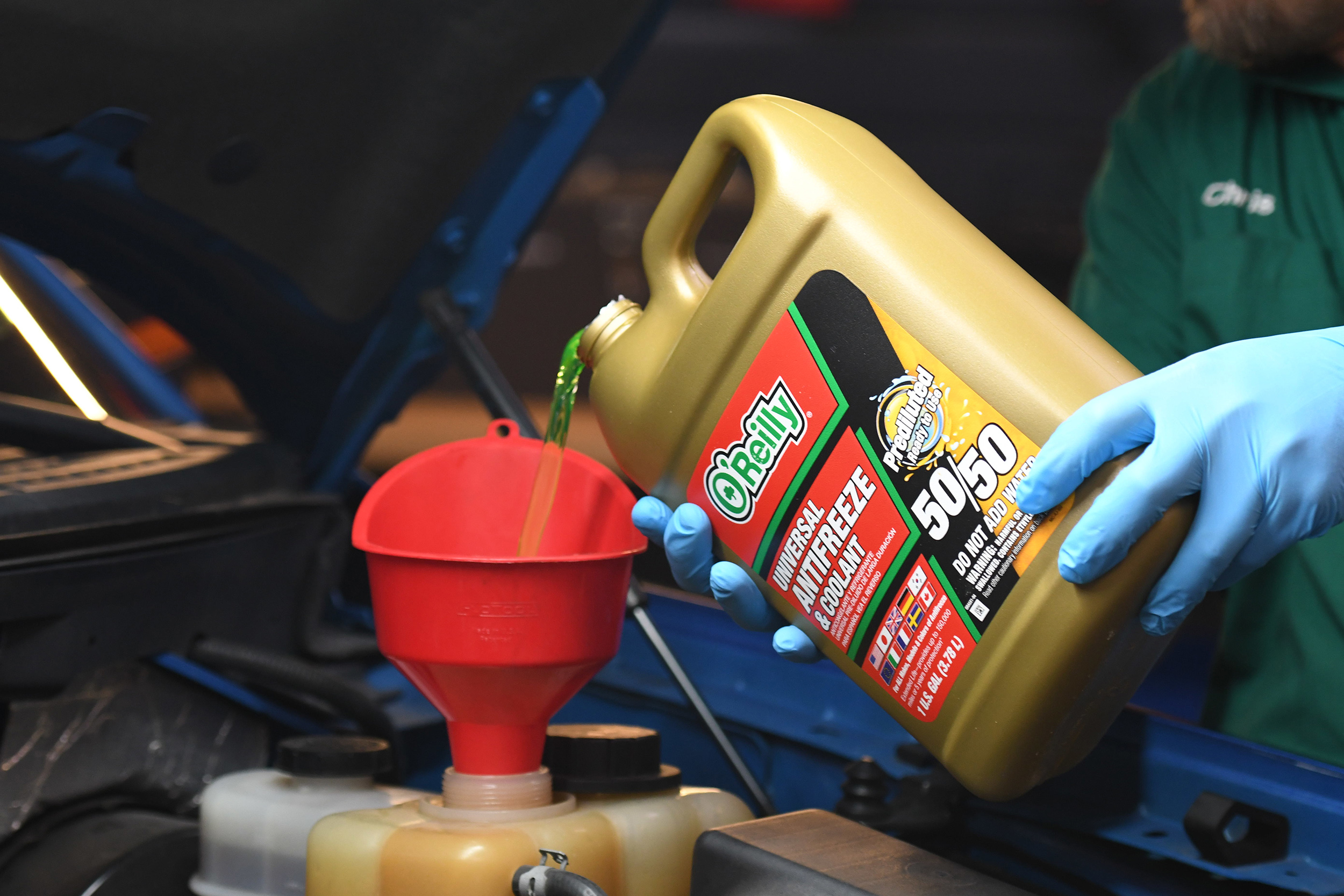 Image shows a bottle of O'Reilly Auto Parts antifreeze/coolant being added to the engine through a funnel.