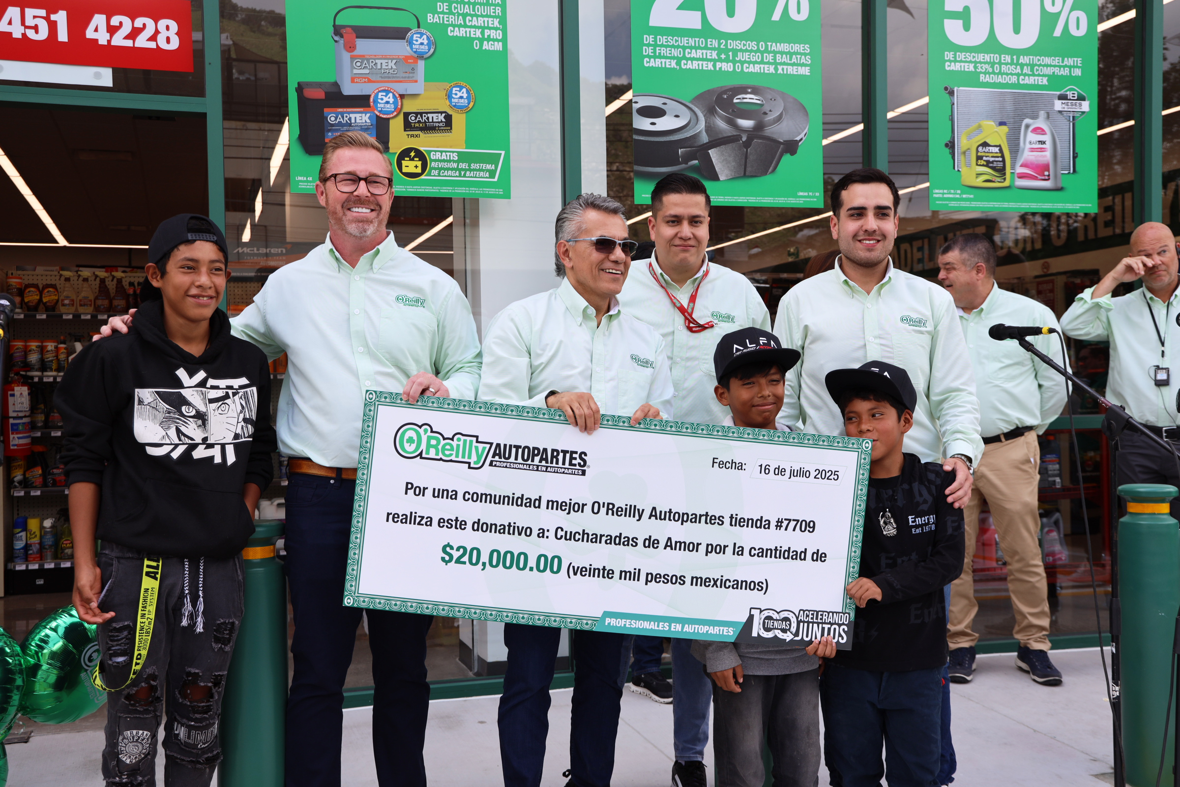 Adults and children hold a very large check during the celebration of O'Reilly Auto Parts reaching 100 stores in Mexico. The money will support a local nonprofit that provides educational support to economically disadvantaged children.