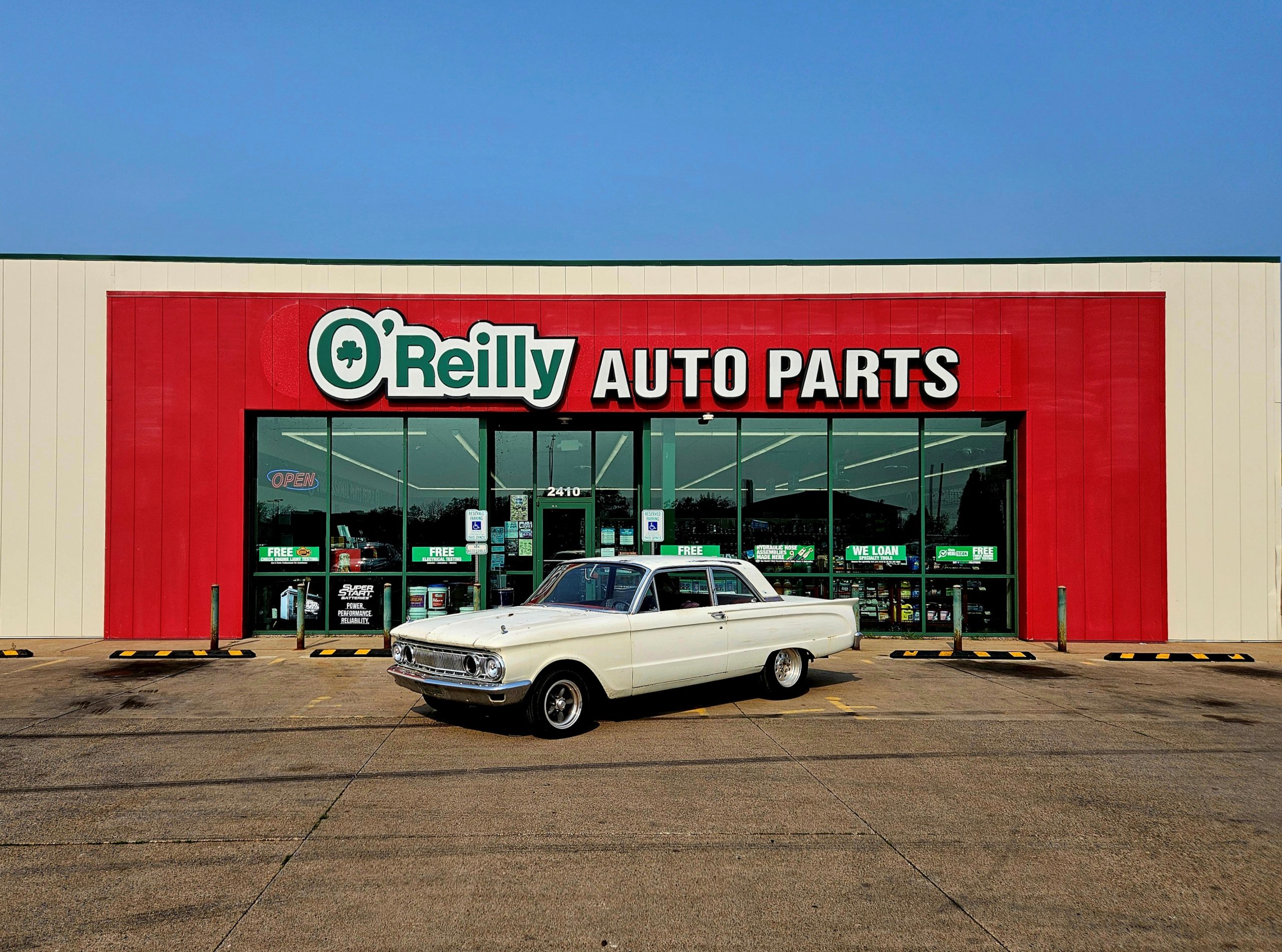 white classic Comet parked in front of O'Reilly Auto Parts storefront
